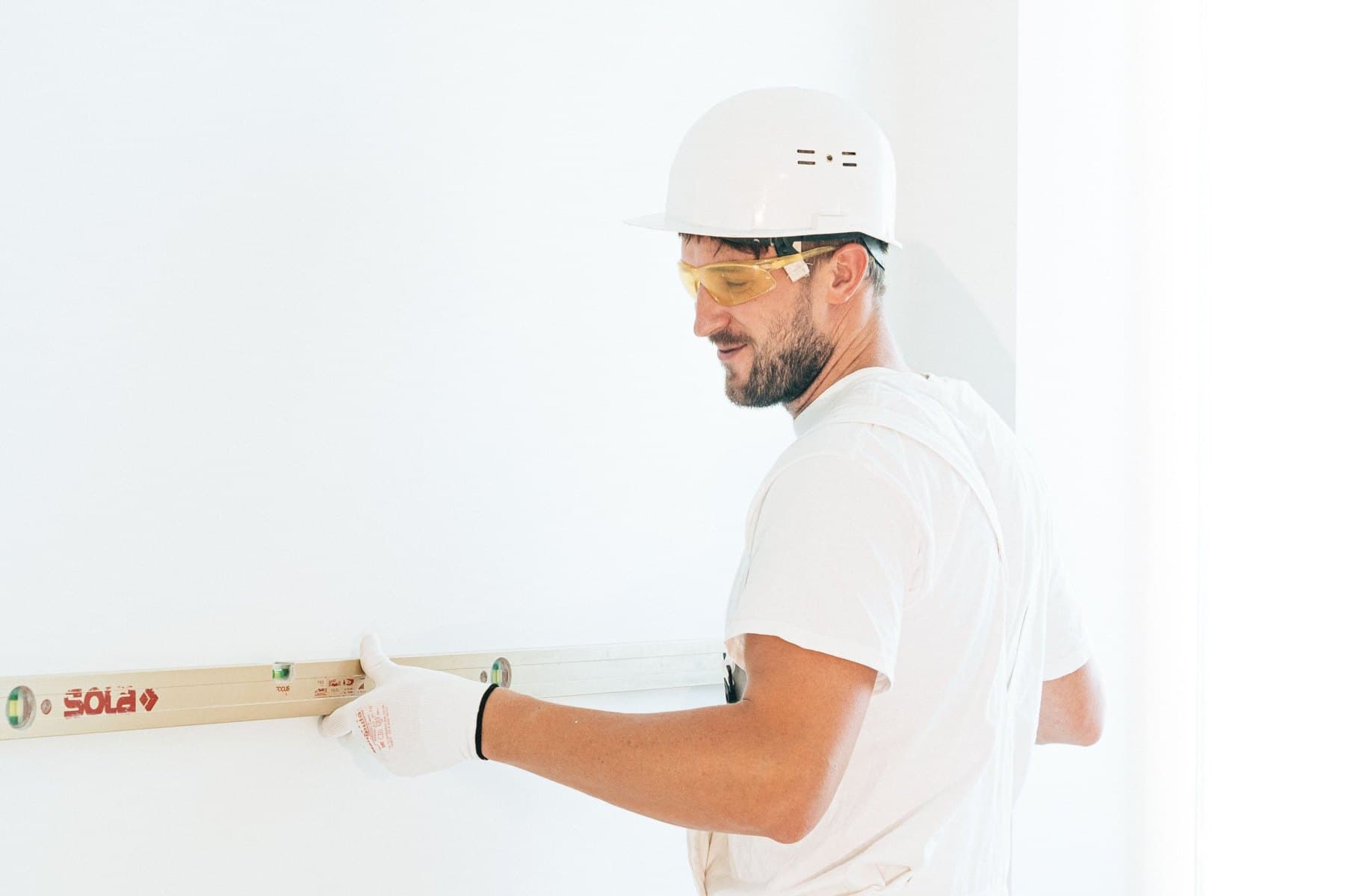 Un artisan en tenue blanche pose un niveau contre un mur
